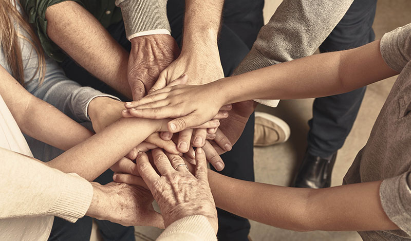 Picture centered on overlapping stacked hands together from several people, indicating togetherness and teamwork