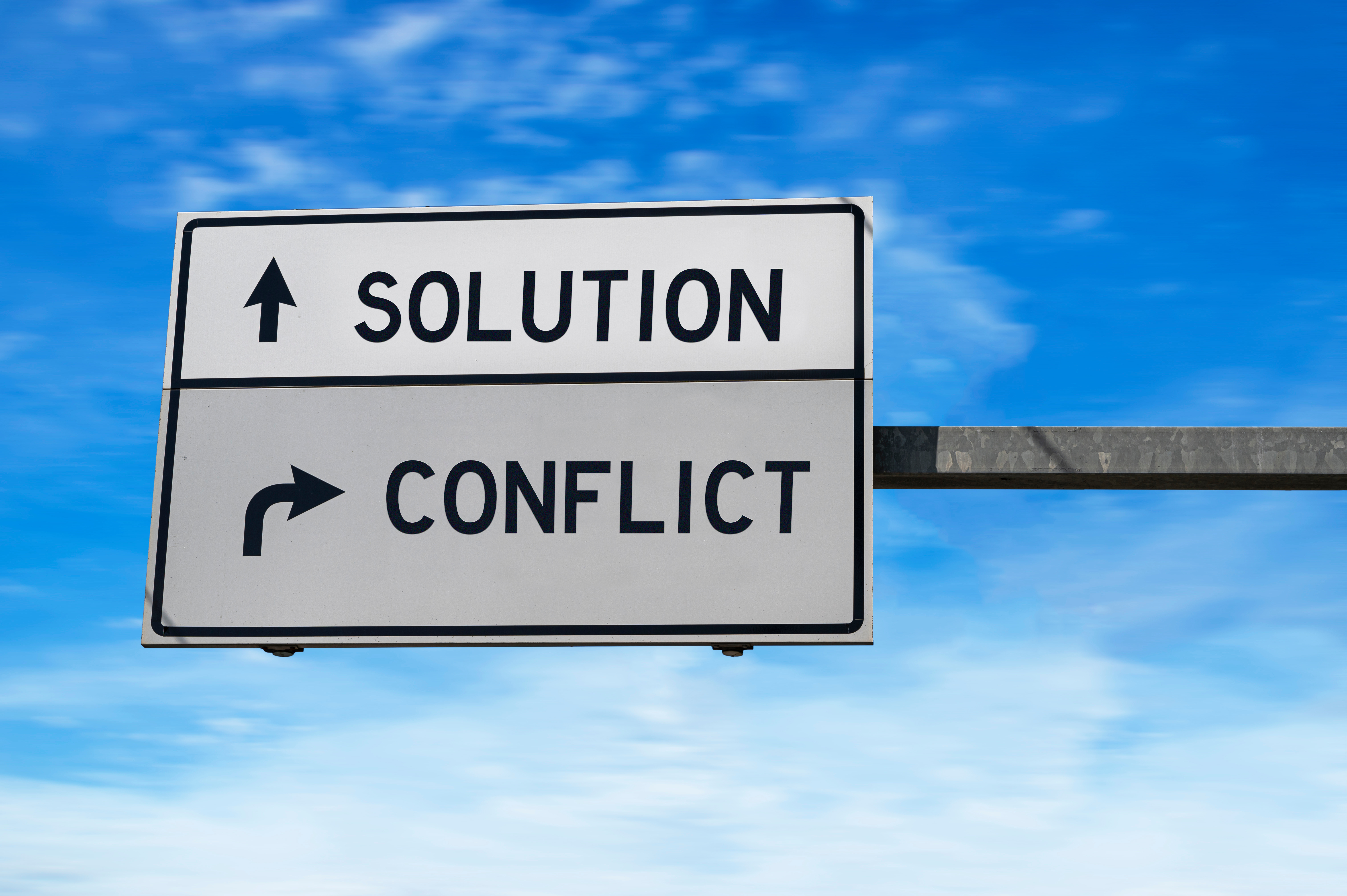 Mediation Traffic Signs - two white street signs with arrow on metal pole, with text indicating Solution and Conflict as two directional options with Arrows. Blue sky background.